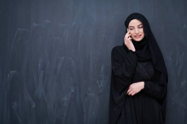 Genç, modern Müslüman iş kadını siyah karatahtanın önünde tesettürlü kıyafetler giyiyor.