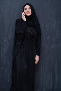 Genç, modern Müslüman iş kadını siyah karatahtanın önünde tesettürlü kıyafetler giyiyor.