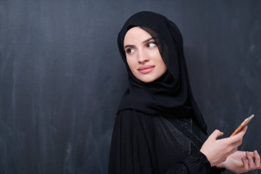 Genç, modern Müslüman iş kadını siyah karatahtanın önünde tesettürlü kıyafetler giyiyor.