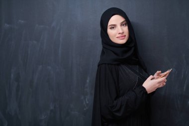Genç, modern Müslüman iş kadını siyah karatahtanın önünde tesettürlü kıyafetler giyiyor.