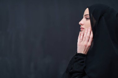 Güzel Müslüman kadın portresi, tesettürlü, geleneksel dua eden, modern İslami modayı ve Ramazan Kareem kavramını temsil eden siyah karatahta izole edilmiş dua eden bir jest içinde.