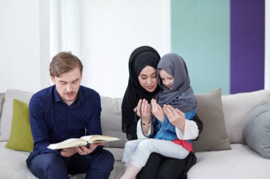 Geleneksel Müslüman aile ebeveynleri ve çocukları evde bir Ramazan şöleni sırasında iftar yemeğinden önce Kuran okuyup birlikte dua ediyorlar.