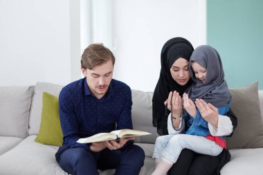Geleneksel Müslüman aile ebeveynleri ve çocukları evde bir Ramazan şöleni sırasında iftar yemeğinden önce Kuran okuyup birlikte dua ediyorlar.