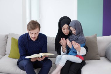 Geleneksel Müslüman aile ebeveynleri ve çocukları evde bir Ramazan şöleni sırasında iftar yemeğinden önce Kuran okuyup birlikte dua ediyorlar.