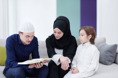 Geleneksel Müslüman aile ebeveynleri ve çocukları evde bir Ramazan şöleni sırasında iftar yemeğinden önce Kuran okuyup birlikte dua ediyorlar.