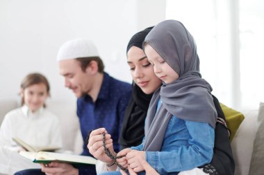 Geleneksel Müslüman aile ebeveynleri ve çocukları evde bir Ramazan şöleni sırasında iftar yemeğinden önce Kuran okuyup birlikte dua ediyorlar.