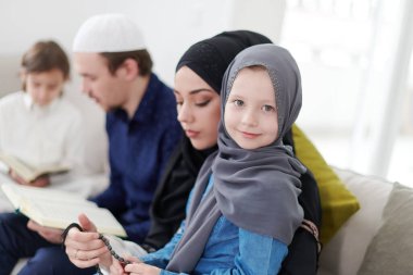 Geleneksel Müslüman aile ebeveynleri ve çocukları evde bir Ramazan şöleni sırasında iftar yemeğinden önce Kuran okuyup birlikte dua ediyorlar.