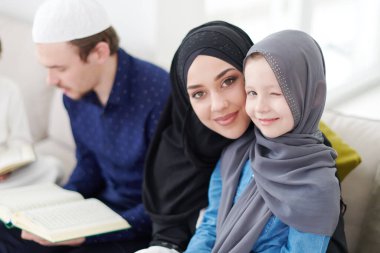 Geleneksel Müslüman aile ebeveynleri ve çocukları evde bir Ramazan şöleni sırasında iftar yemeğinden önce Kuran okuyup birlikte dua ediyorlar.