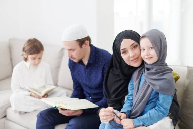 Geleneksel Müslüman aile ebeveynleri ve çocukları evde bir Ramazan şöleni sırasında iftar yemeğinden önce Kuran okuyup birlikte dua ediyorlar.