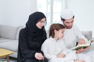 Geleneksel Müslüman aile ebeveynleri ve çocukları evde bir Ramazan şöleni sırasında iftar yemeğinden önce Kuran okuyup birlikte dua ediyorlar.