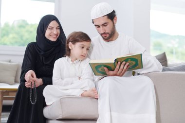 Geleneksel Müslüman aile ebeveynleri ve çocukları evde bir Ramazan şöleni sırasında iftar yemeğinden önce Kuran okuyup birlikte dua ediyorlar.