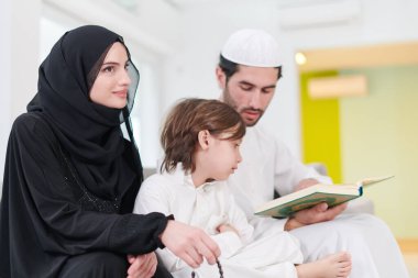 Geleneksel Müslüman aile ebeveynleri ve çocukları evde bir Ramazan şöleni sırasında iftar yemeğinden önce Kuran okuyup birlikte dua ediyorlar.