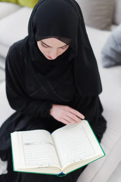 若い伝統的なイスラム教徒の女性は家でラマダーンの宴の間にイフタールディナーの前にソファの上でクルアーンを読む — ストック写真