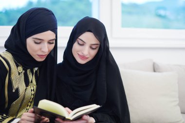 Genç geleneksel Müslüman kadınlar evde ramazan ziyafeti sırasında iftar yemeğinden önce kanepede Kur 'an okuyorlar.
