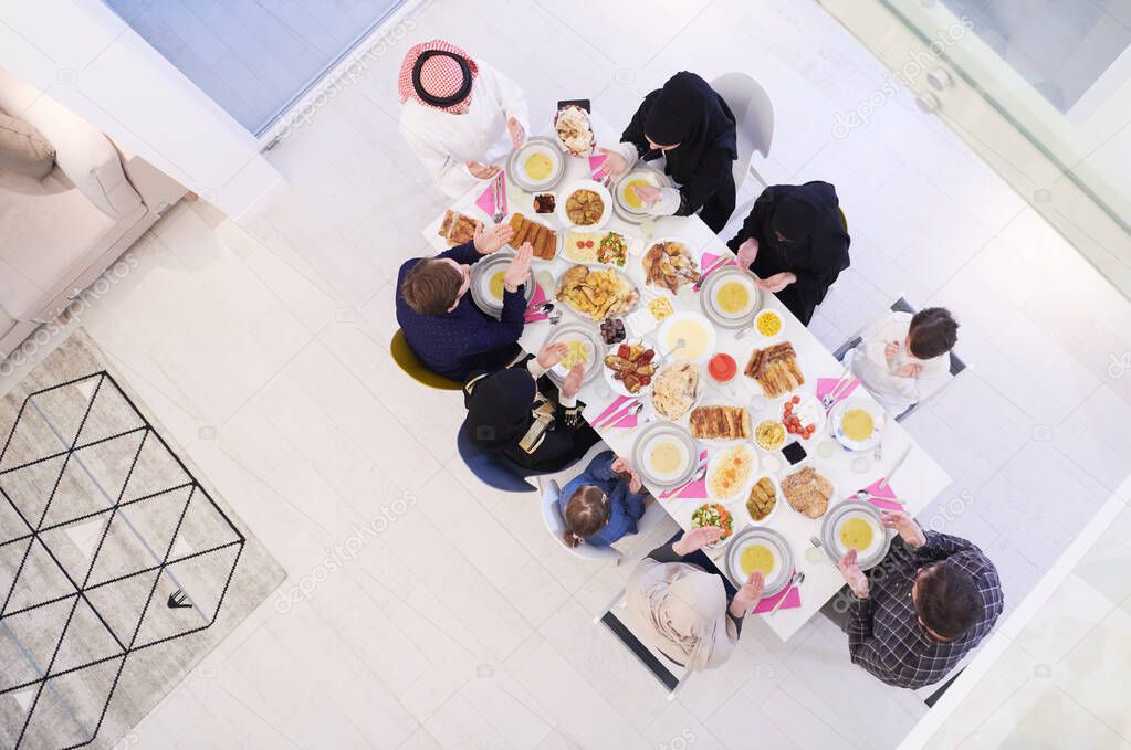 Eid Mubarak Muslim people praying before iftar dinner. Eating traditional food during Ramadan feasting month at home. The Islamic Halal Eating and Drinking at modern western Islamic family top view