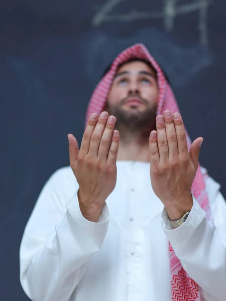 伝統的な服を着た若いアラビア人男性が伝統的な神への祈りをし 現代のイスラム教のファッションとラマダーン カレームの概念を表す黒い黒板の前で手をつないで祈り続ける — ストック写真