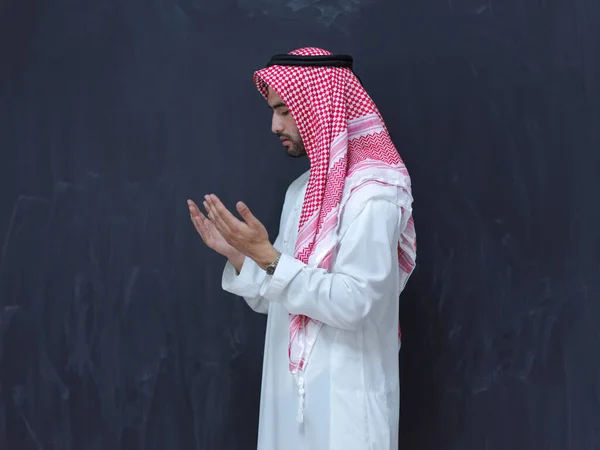 伝統的な服を着た若いアラビア人男性が伝統的な神への祈りをし 現代のイスラム教のファッションとラマダーン カレームの概念を表す黒い黒板の前で手をつないで祈り続ける — ストック写真