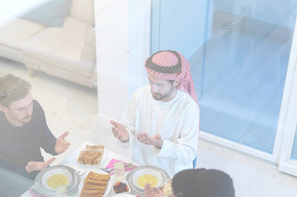 Eid Mubarak Muslim people praying before iftar dinner. Eating traditional food during Ramadan feasting month at home. The Islamic Halal Eating and Drinking at modern western Islamic family