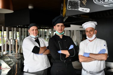 Karışık yarış ekibi portresi. Mutfakta birlikte duran grup şeflerinin portresi. Koruyucu tıbbi maske ve eldiven takıyorlar.