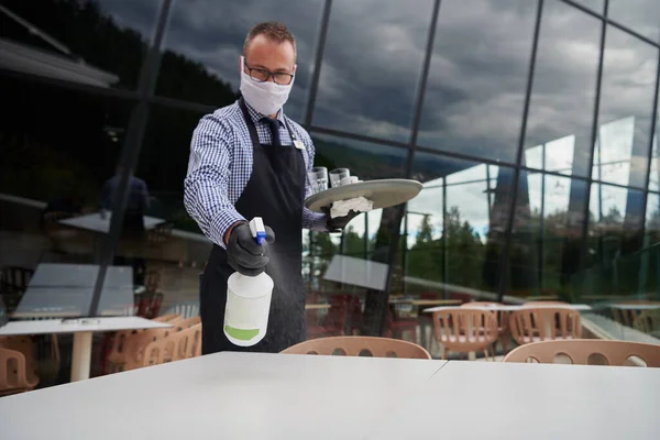 Číšník Čistí Stůl Dezinfekčním Sprejem Restauraci Ochrannou Lékařskou Maskou Rukavicemi — Stock fotografie