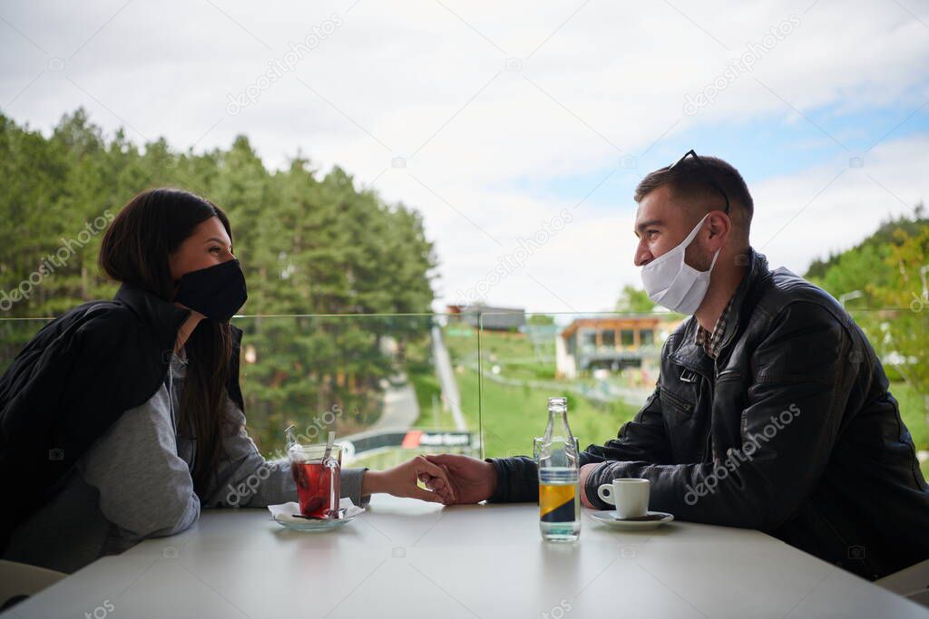 couple in restaurant wearing medical protective face masks  coronavirus protection social distancing and prevention  concept male smoking and checking smart phone
