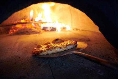 Rustik pizza fırının sıcak olduğu yerden kalkıyor. Aşçı onları çıkarmak için özel kürek kullanıyor. Bu restoranın özel ahşap fırını var.