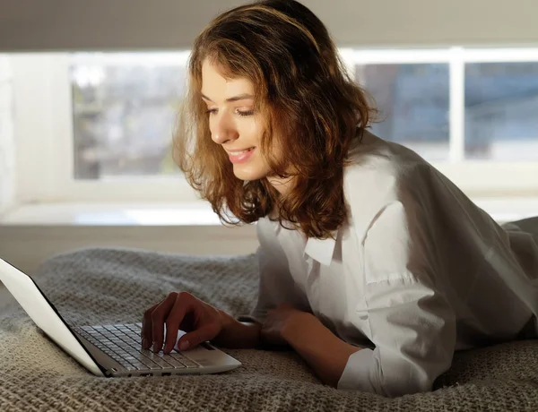 Mujer joven en casa en la cama usando el ordenador portátil . —  Fotos de Stock