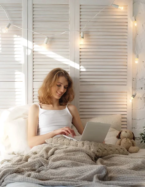 Молода жінка вдома в ліжку за допомогою ноутбука . — стокове фото