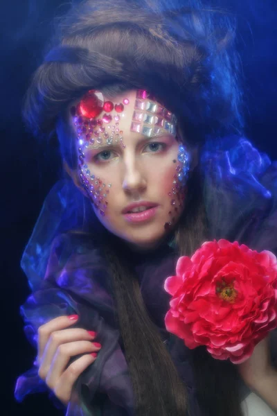 Ung kvinna med konstnärliga visage innehar stor röd blomma — Stockfoto