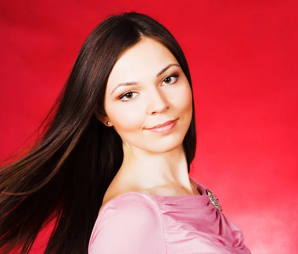 Junge Frau mit langen Haaren posiert im Studio vor rotem Hintergrund — Stockfoto