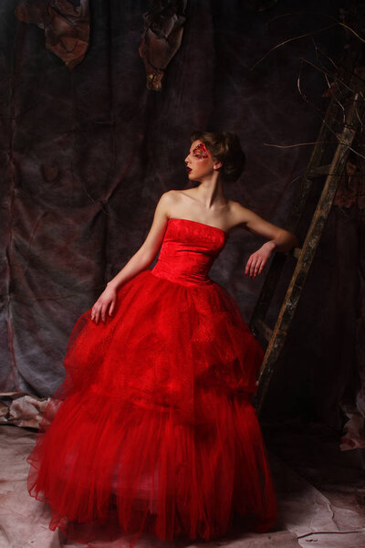 Portrait of a beautiful blond woman in red dress. Creative make up and hairstyle. Shot in a fantasy house.