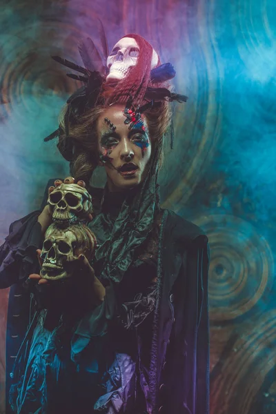 Een jonge heks met een schedel. Heldere make-up en rook-Halloween thema. — Stockfoto