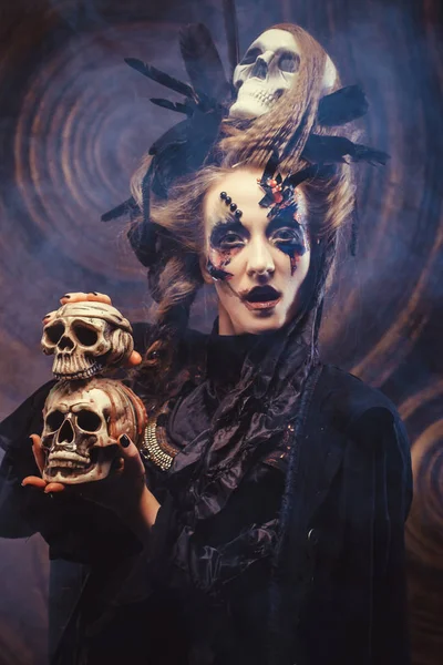若い魔女は頭蓋骨を持ってる。明るいメイクと煙-ハロウィンのテーマ. — ストック写真