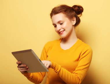 Sarı arka planda tablet bilgisayarı olan genç bir kadın.