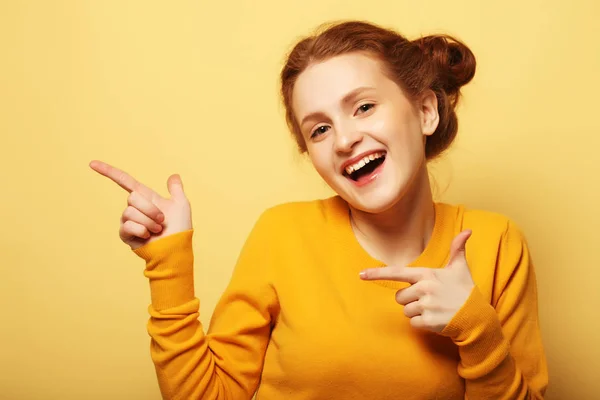 Portrait of a pretty girl  pointing finger away over yellow  bac — Stock Photo, Image