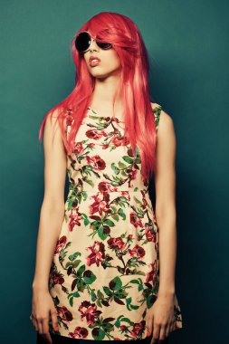 Mavi arka planda pembe saçlı ve büyük güneş gözlüklü manken.