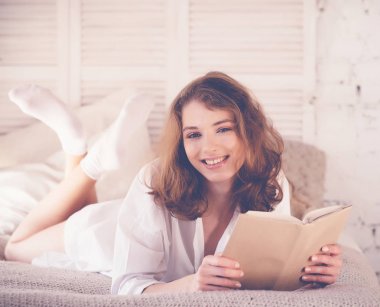 Yatakta kitap okuyan güzel sarışın kadın. Rahatlatıcı kavram