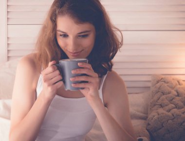 Evde yatakta kahve içen güzel bir kadın.