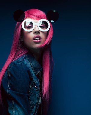 Mavi arka planda pembe saçlı ve büyük güneş gözlüklü manken.