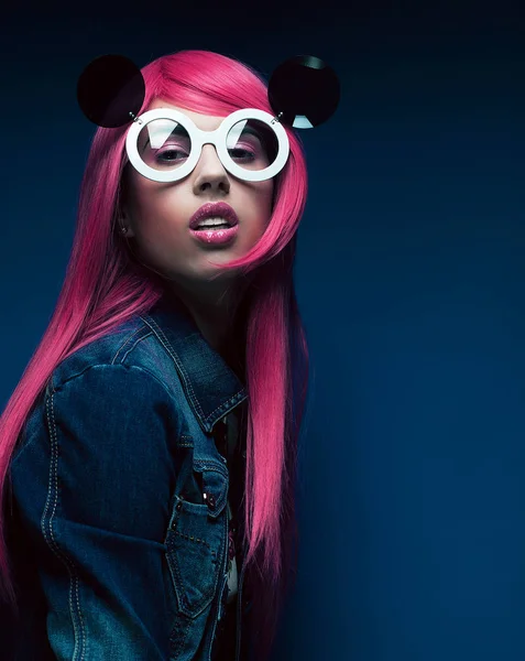 Mavi arka planda pembe saçlı ve büyük güneş gözlüklü manken.