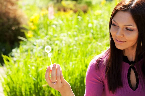 Girl blow soap bubble against a background grass — Stock Photo, Image