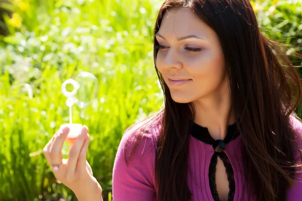 Girl blow soap bubble against a background grass — Stock Photo, Image