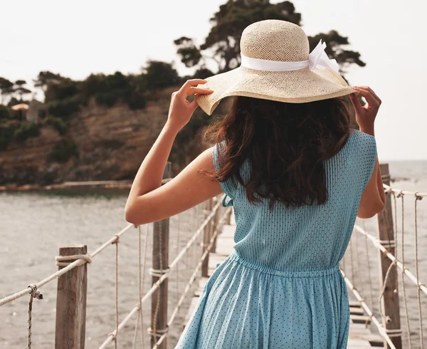 Jovem mulher em vestido de verão em pé na ponte e segurando palha — Fotografia de Stock