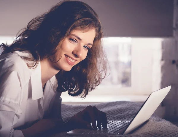 Egy nő fekszik az ágyon egy laptoppal. Életmód és az emberek koncept — Stock Fotó