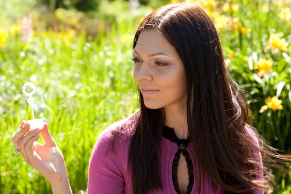 Girl blow soap bubble against a background grass — Stock Photo, Image