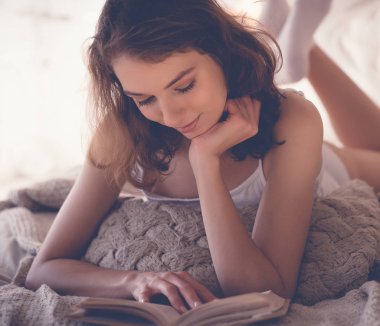 Yatakta kitap okuyan güzel sarışın kadın. Rahatlatıcı kavram
