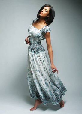 Gri sırt çantasının üzerinden atlayan şifon elbiseli çekici bir kadın.