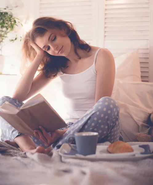 Дівчина в ліжку читає і п'є каву — стокове фото