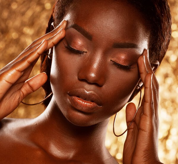 Fashion studio portrait of an extraordinary beautiful african american model with closed eyes, perfect smooth glowing mulatto skin, bright make up, over golden background