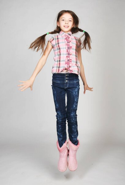 маленькая девочка прыгает на сером фоне